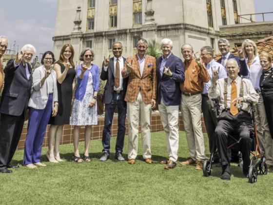 group of people posing while smiling and holding hook 'em hand signal