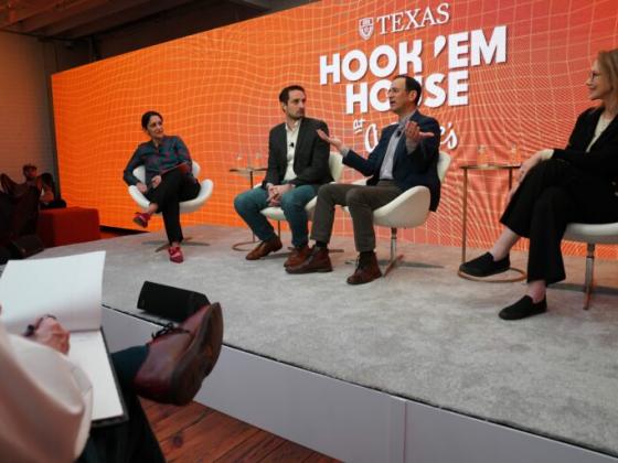 four people sitting in chairs for a panel with a crowd in the foreground