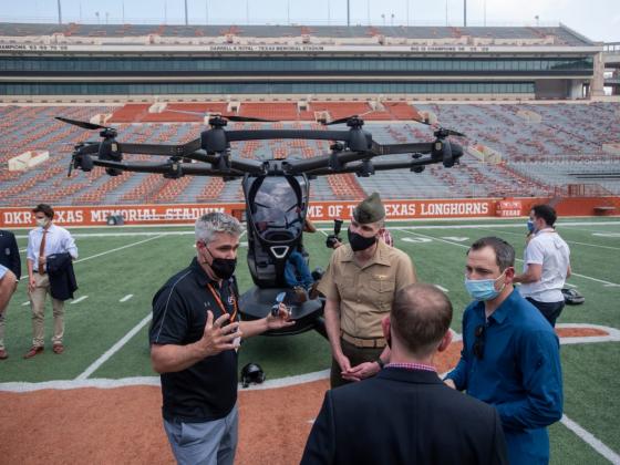 Marine General Gary Thomas on football field talking to a group of people with a car-sized eVTOL aircraft in background