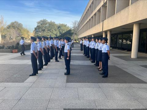 Uniformed ROTC cadets standing in formation outdoors on a campus walkway during a military drill or ceremony.