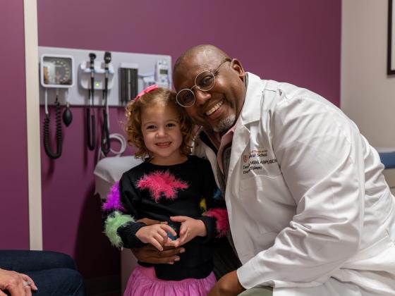 A child and a doctor smile for a photo in an exam room.