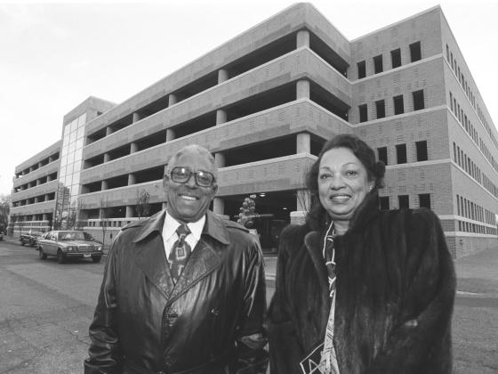 A black and white photo of two people smiling in front of a parking garage in 1994.