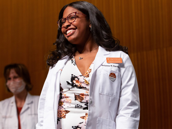 Brianna Earskine stands, smiling in white lab coat