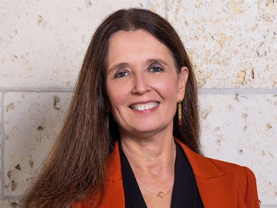 A woman wearing a burnt orange blazer smiles while posing for a photo in front of a limestone wall.