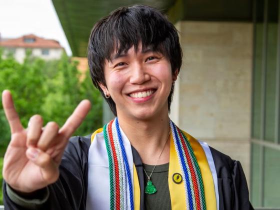 Portrait of Dat Duong in regalia holding Hook 'em horns hand symbol