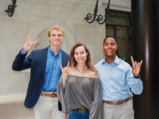Three students smile for a photo while holding up the Hook ’em, Horns hand sign.