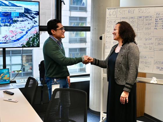 Two people shaking hands in front of a whiteboard.