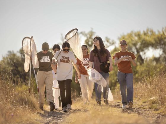 Students wearing Texas Science T-shirts conduct fieldwork and use nets to collect insects.