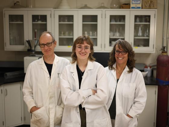Three people stand together in a lab wearing white lab coats