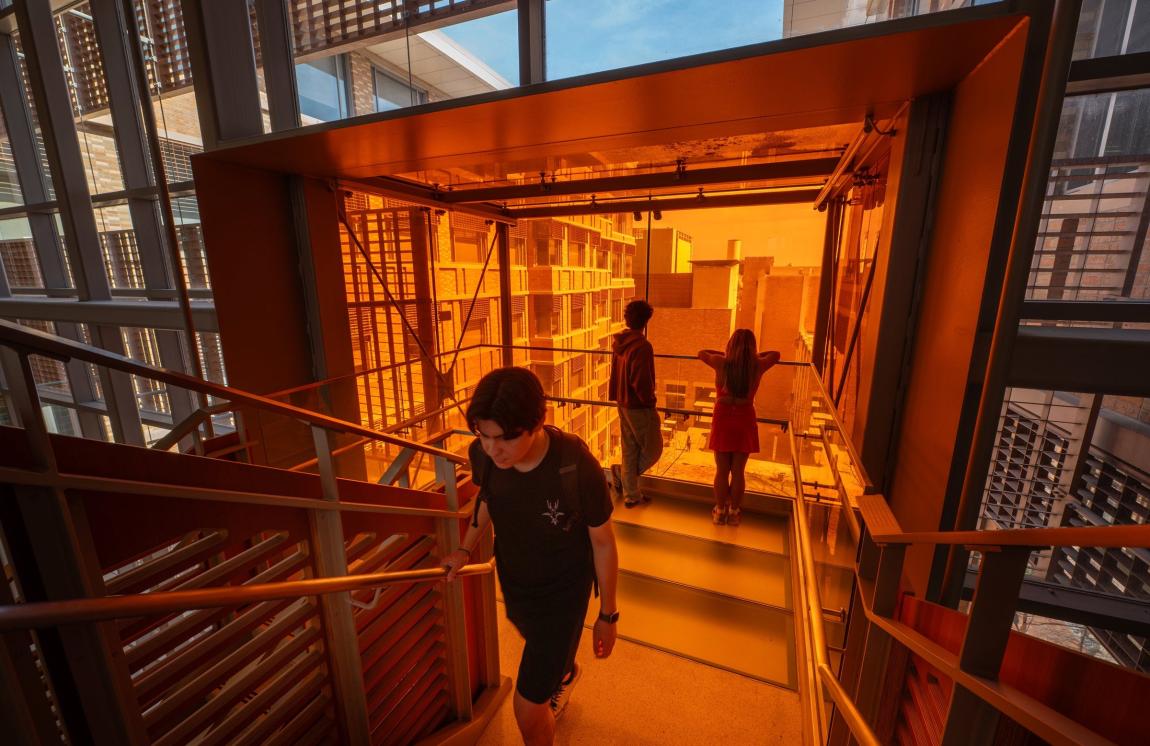 A student walks up a staircase with orange lighting.