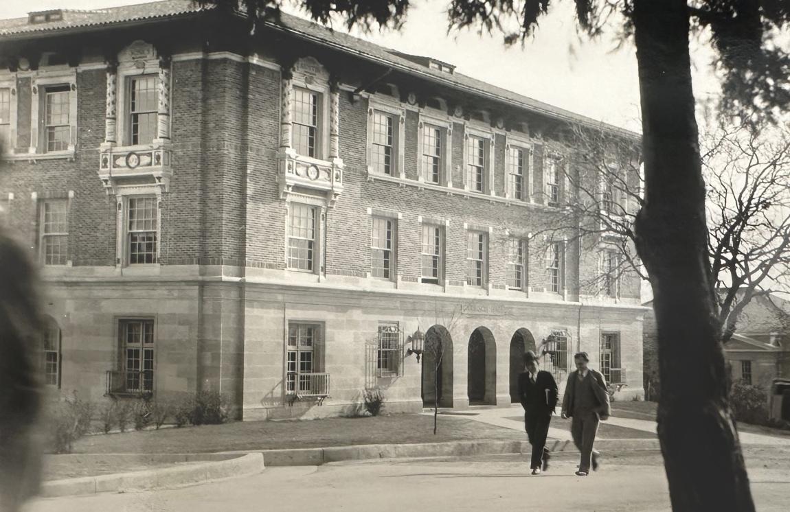 An archival photo of two people walking past Garrison Hall on the University of Texas at Austin campus.