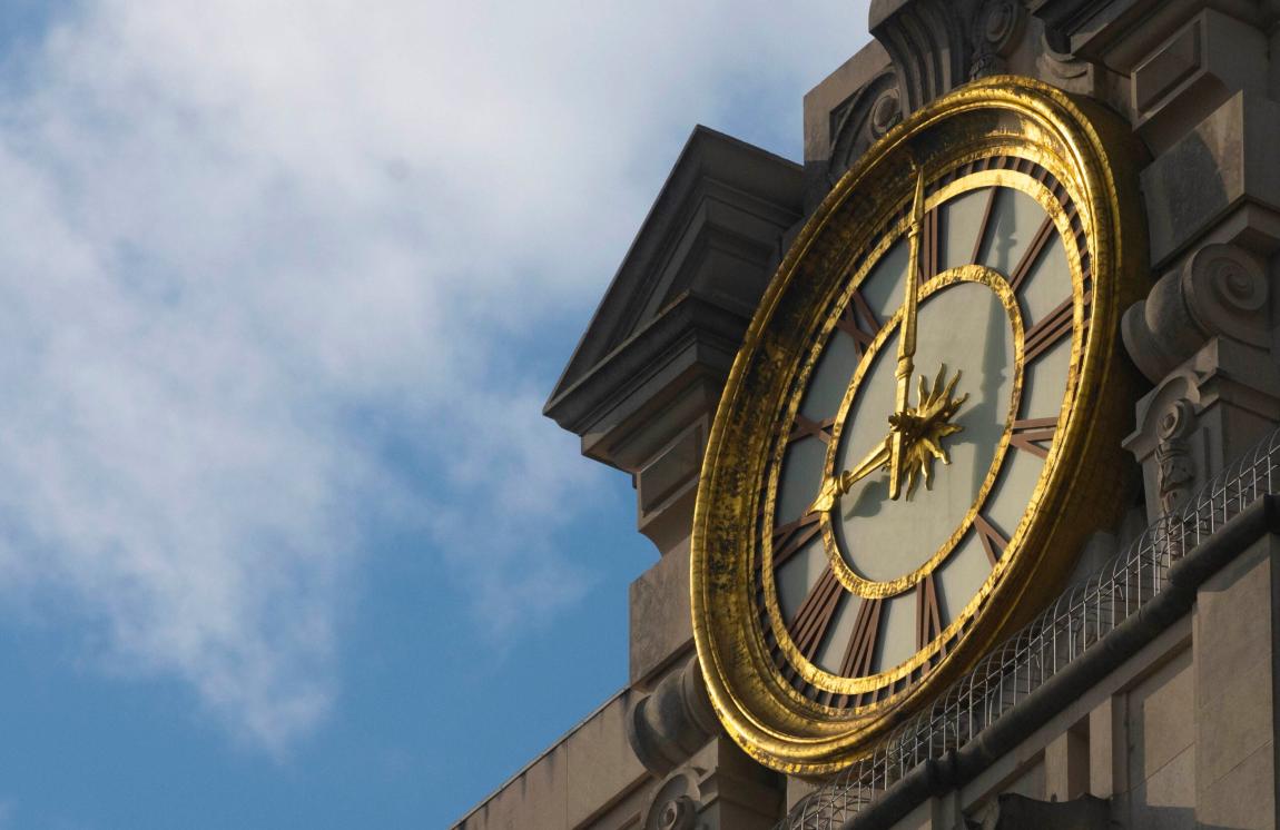 A close-up of the clock at the top of the University of Texas at Austin Tower with clouds in the background.
