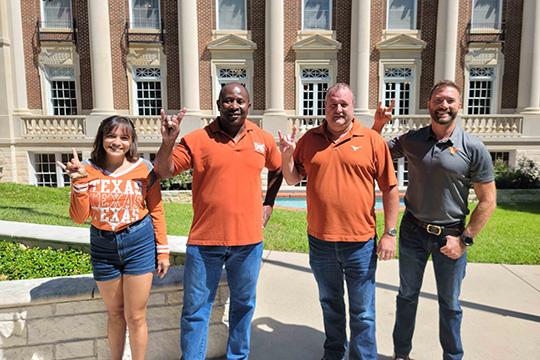 Group of 4 UT Alumni on campus holding up hook 'em hand sign