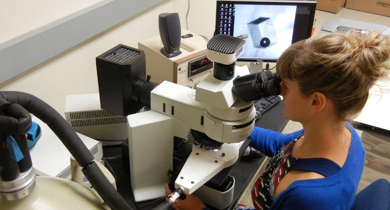 woman at a desk looking into a microscope device