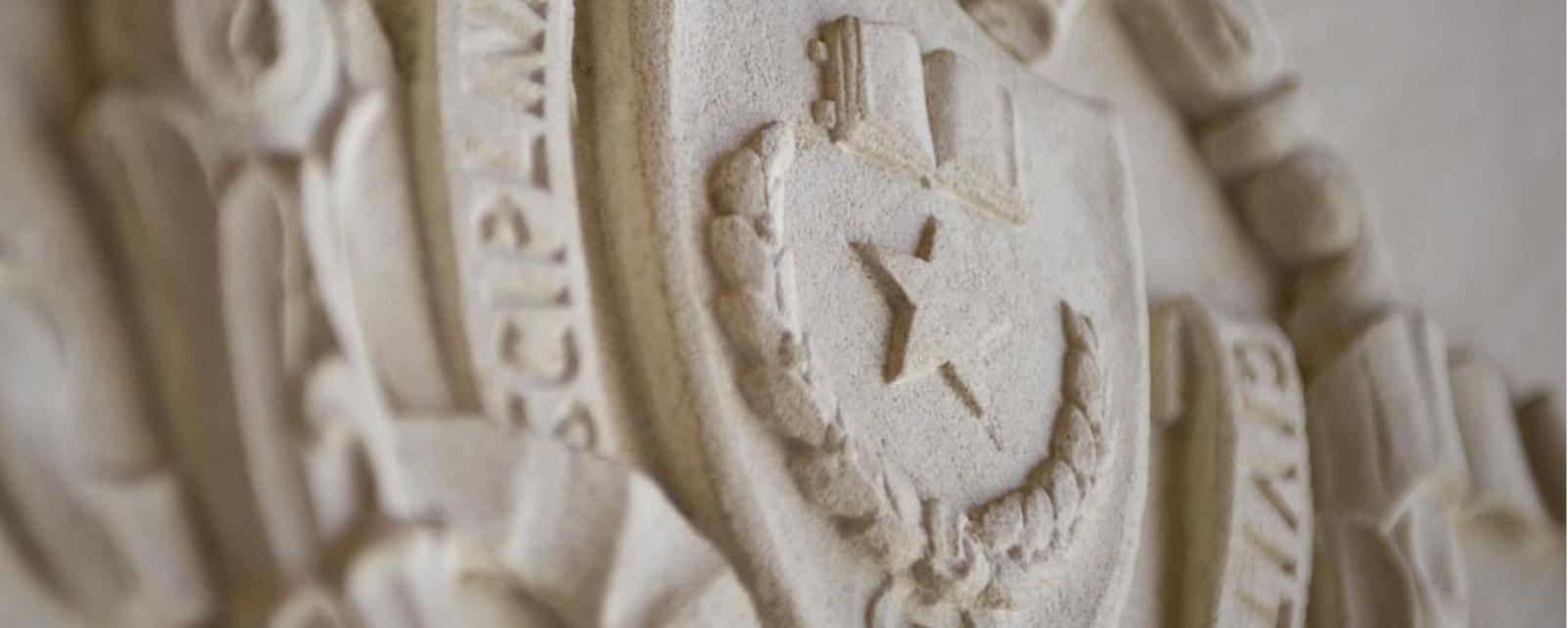 Close up of UT Austin's campus seal carved into cream colored stone.