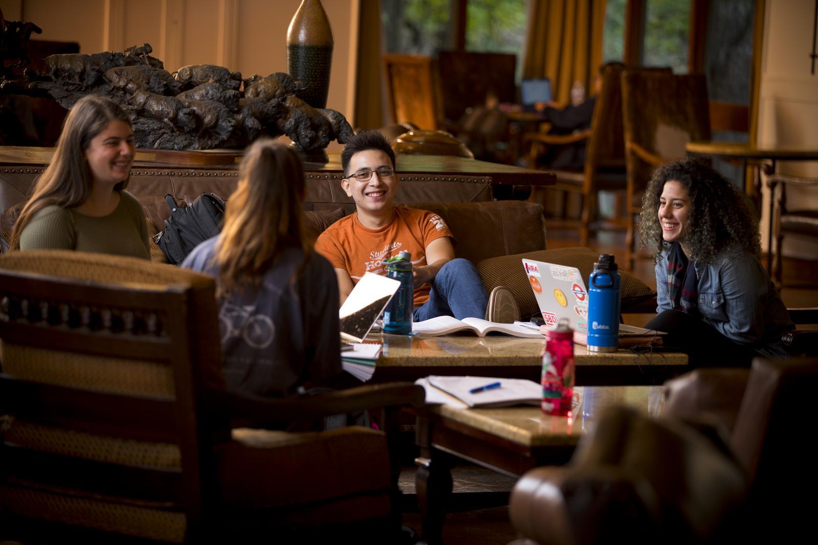 A group of students smile while talking around a coffee table in a lounge.