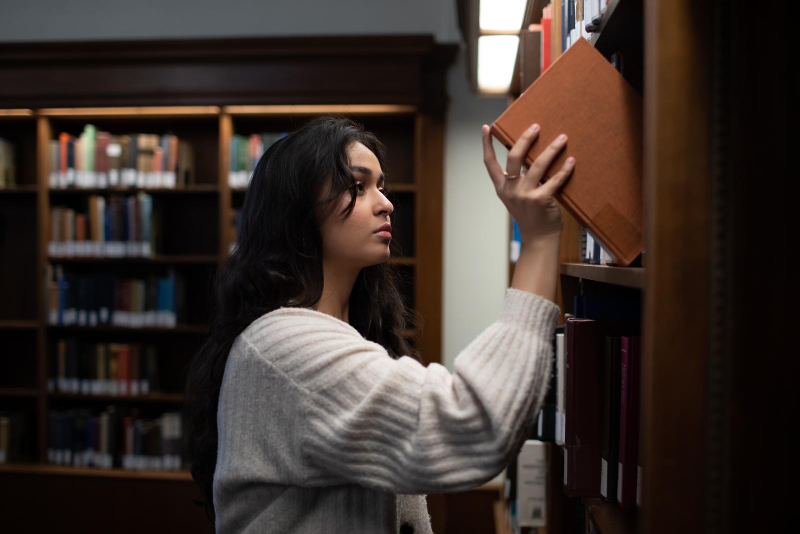 A woman pulls a book off of a library shelf.