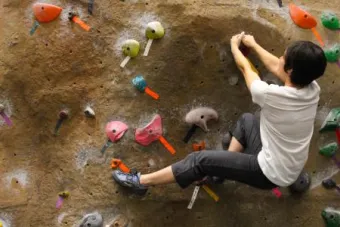 A man climbs on a brown rock wall at UT. His hands hold onto one rock while his foot stretches out to reach the rocks below him.
