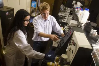 A graduate student works with a professor who points out what they should adjust on a piece of complicated machinery.
