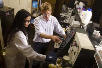 A graduate student works with a professor who points out what they should adjust on a piece of complicated machinery.