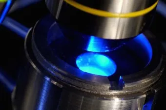 Close up of the top of a microscope with a glowing blue light.
