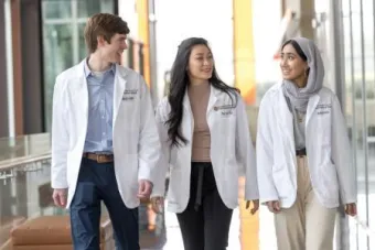 three medical student in white coats walk together
