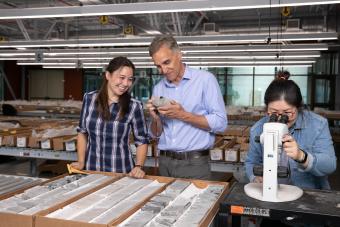 A professor and two students examine rock samples in a lab.