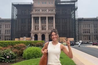 A student stands in front of the Texas Capitol.