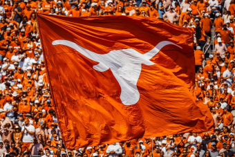 A burnt orange flag with a white Longhorn silhouette waves in front of a crowd.