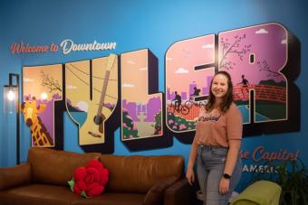 A student stands in front of a mural that reads "Welcome to Downtown Tyler"