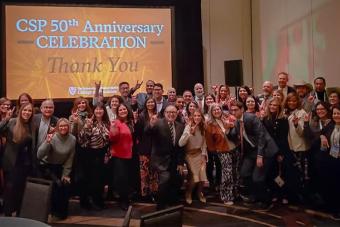 A group of people pose for a photo in front of a screen that reads "CSP 50th Anniversary / Thank You"