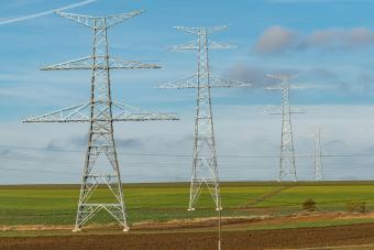 High-voltage power transmission towers standing in a rural field under a blue sky.