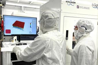 Two researchers wearing personal protective equipment work on a computer in a cleanroom.
