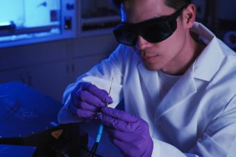 A researcher wearing goggles, a white lab coat and purple gloves examines a fiber probe.