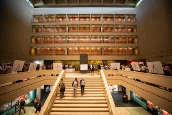 The interior atrium of the UT The Institute for Military & Veteran Family Wellness, showing the grand staircase, multi-story open shelving, and several people moving through the space.