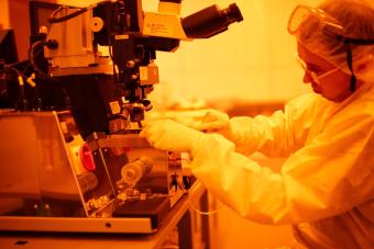 A student works on a microscope in a cleanroom with amber lighting.