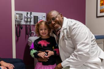 A child and a doctor smile for a photo in an exam room.