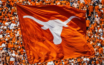 A burnt orange flag with a white Longhorn silhouette waves in front of a crowd.