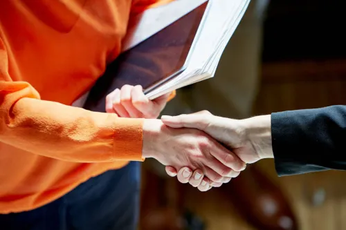 A handshake is exchanged between two professionally dressed individuals wearing orange and black respectively.