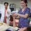 Students practice nursing in lab. One wears scrubs and another a lab coat while they hold the arm of one student pretending to be a patient.