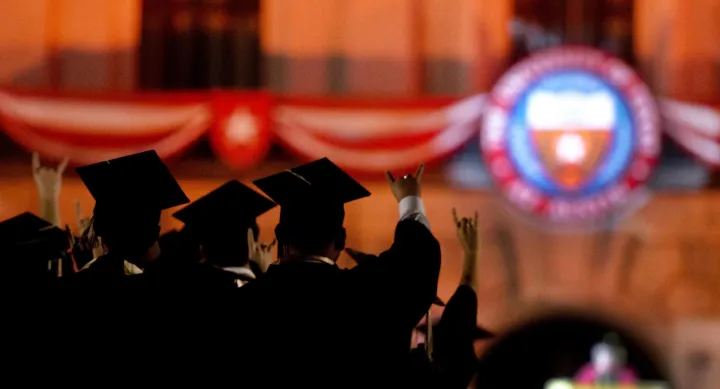 commencement showing graduates with hook 'em horns raised