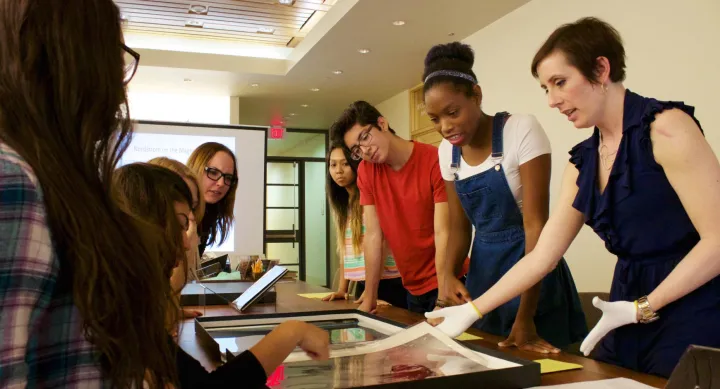 Students observing a professional handle paper research materials with gloves.