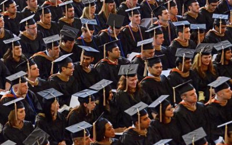Show of graduates wearing their cap and gowns while they sit at a graduation commencement.