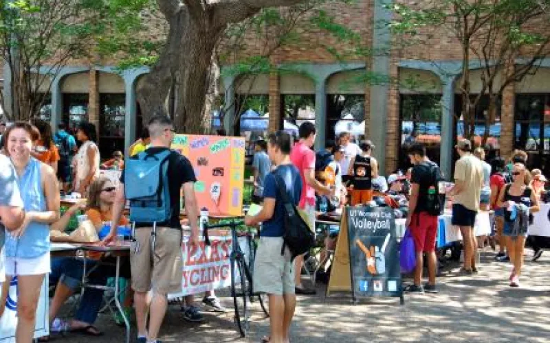 Many different tables for student organizations sit outside on the plaza. They're brightly colored with banners advertising their organizations, and many students walk between the tables and talk to the students behind them.