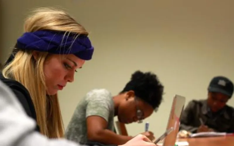 Three students sit at a table writing in journals.