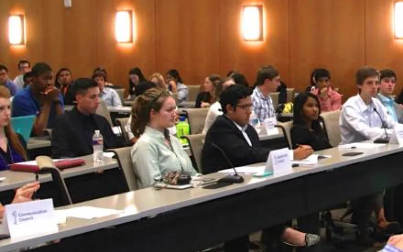 Around fifteen students dressed in professional clothes sit in four rows at a student government meeting. They look towards the front of the room.