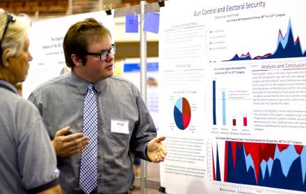  An undergraduate researcher presents his findings using a large-format poster at the Longhorn Research Bazaar