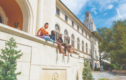 Four students sitting on side bench with UT Tower in the background